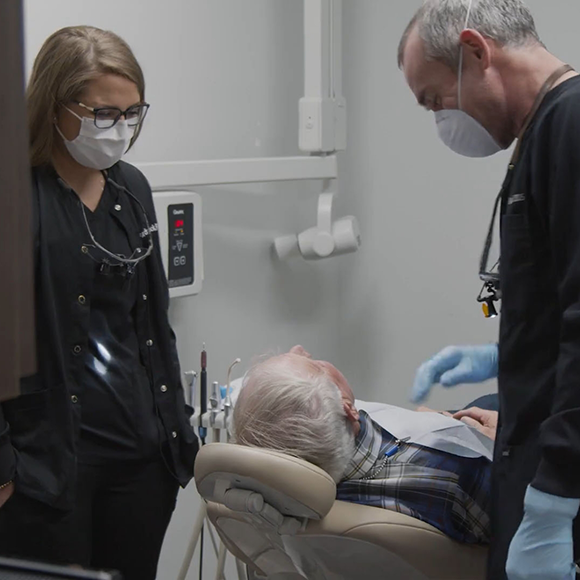 Senior man in the dental chair talking to dentist and assistant