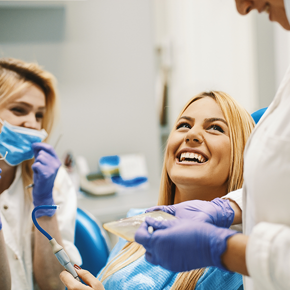 Woman in dental chair grinning up at her dentist