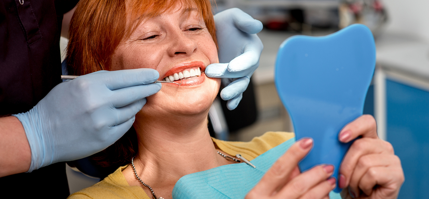 Woman in dental chair admiring her smile in a mirror after cosmetic dentistry in Altavista