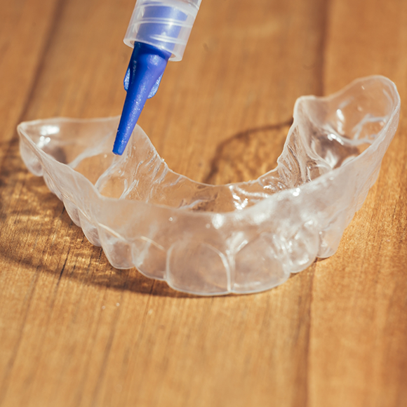 Applicator putting bleaching gel into a teeth whitening tray