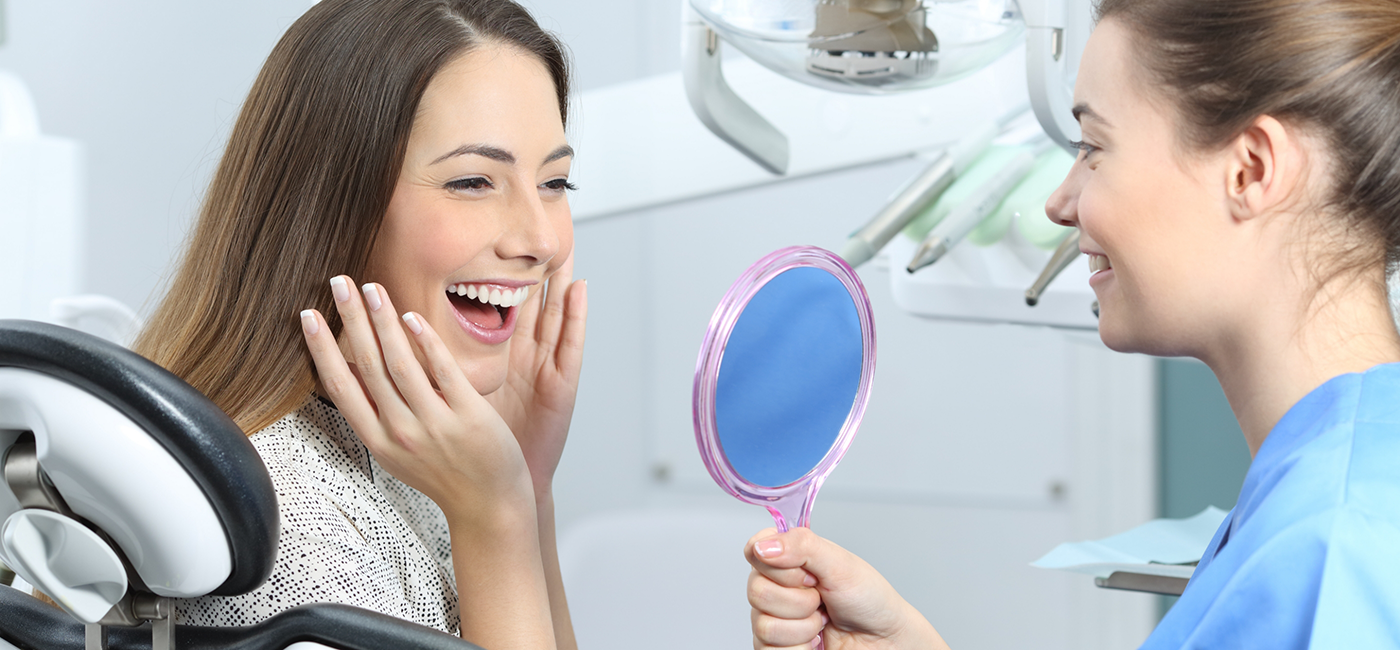 Woman looking at her smile in a mirror after getting dental crowns in Altavista