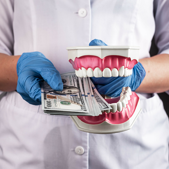 Dentist holding a model of the teeth and several hundred dollar bills