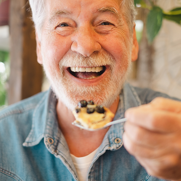 Senior man grinning while holding a spoonful of food