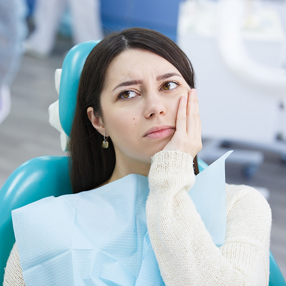 Woman holding her cheek in pain while visiting her emergency dentist