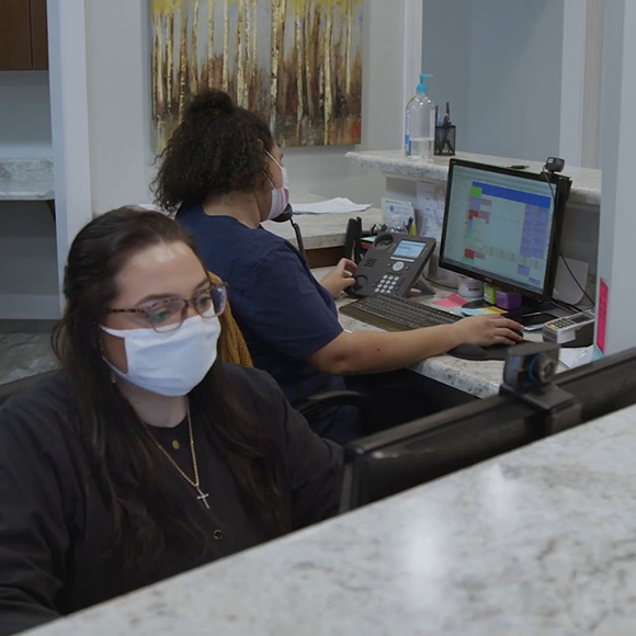 Two dental team members sitting at front desk