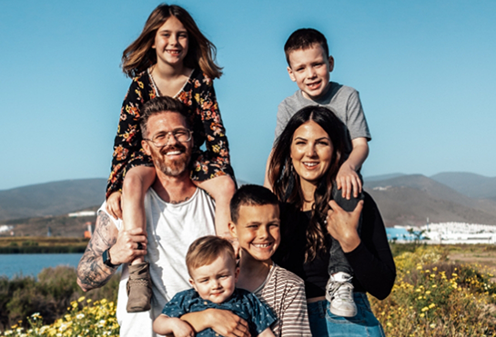 Family of six smiling outdoors on a sunny day