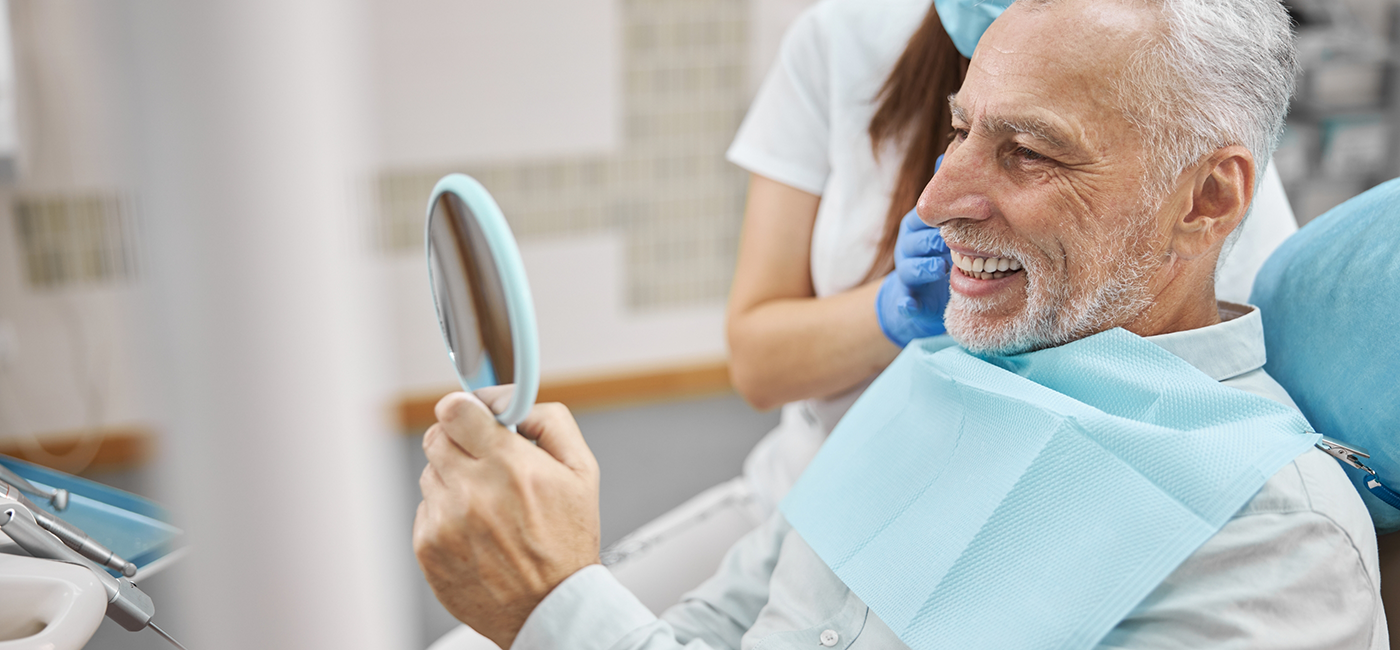 Senior man admiring his smile in a mirror after replacing missing teeth in Altavista