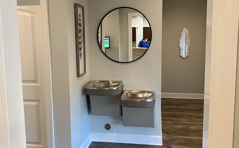 Circular mirror on wall above two water fountains