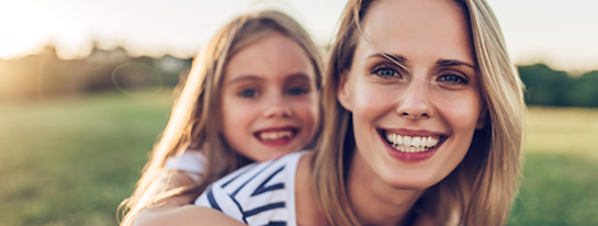 Mother giving her young daughter a piggyback ride outdoors