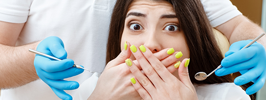 Woman in dental chair looking scared and covering her mouth with her hands