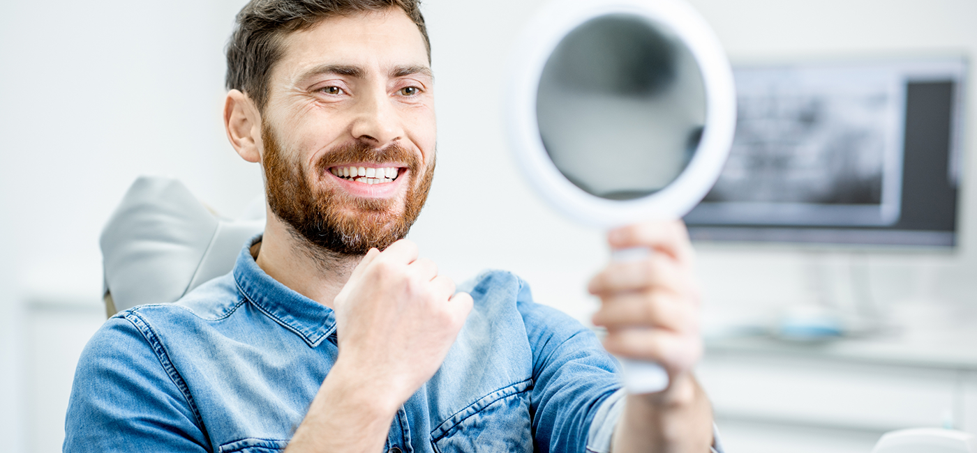 Man admiring his smile in a mirror after restorative dentistry in Altavista