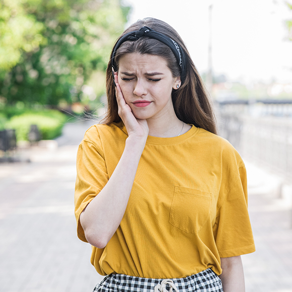 Woman in a yellow blouse wincing and holding her cheek in pain