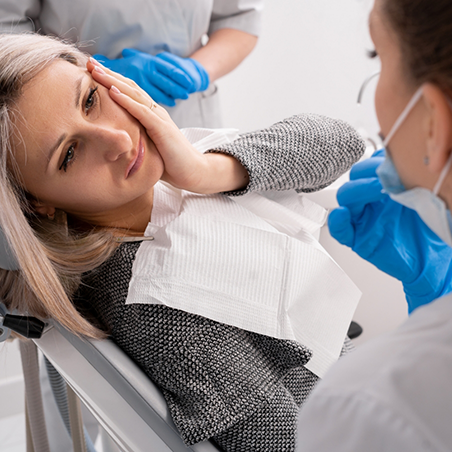 Woman holding her cheek in pain while visiting her dentist