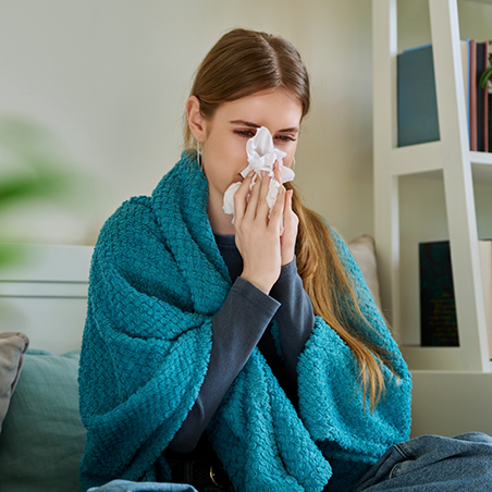 Woman blowing her nose while wrapped in a blanket