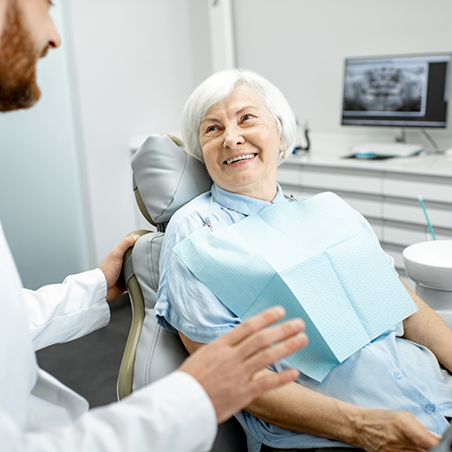 Senior woman in dental chair smiling at her dentist