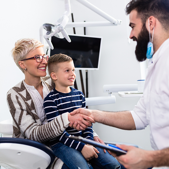 Dentist shaking hands with a woman while her young son sits in her lap