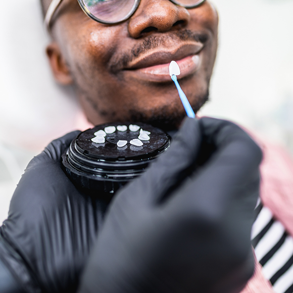 Dentist holding a veneer to a patients smile