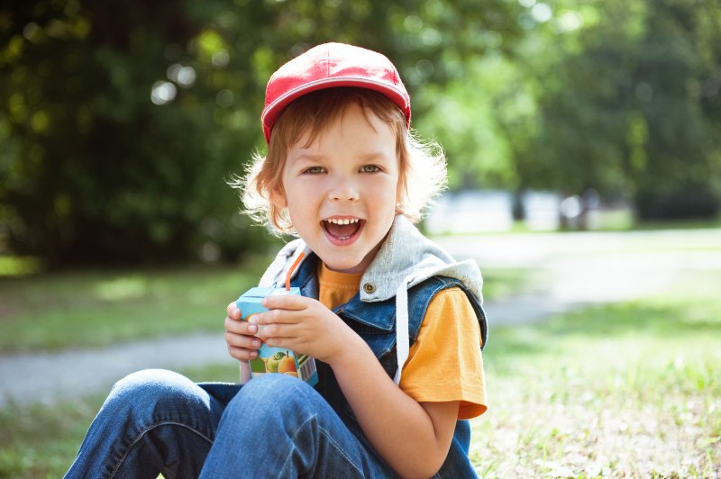 a child sitting outside and drinking a juice box